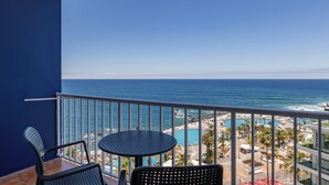 Un balcón con dos sillas y una mesa, con vistas a una playa que tiene una piscina y zona de resort.
