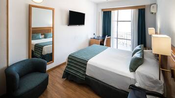 Una habitación de hotel con cama, escritorio, silla, televisión y ventana con cortinas.