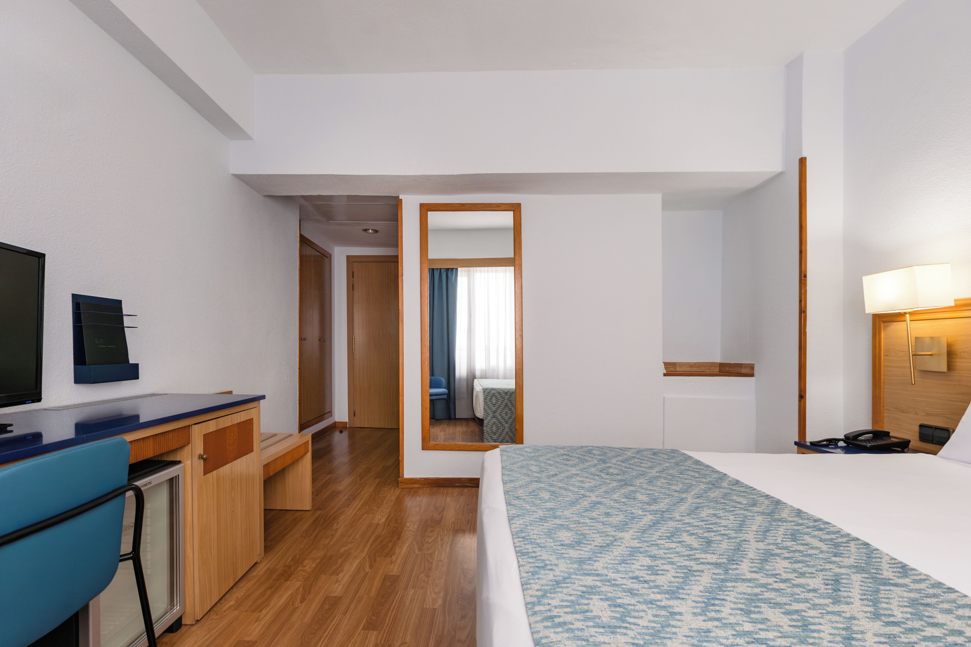 Una habitació d'hotel amb un llit, un escriptori amb un ordinador, una televisió i un mirall.