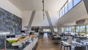 Un comedor moderno con una barra larga, varias mesas y vistas al exterior a través de amplios ventanales.
