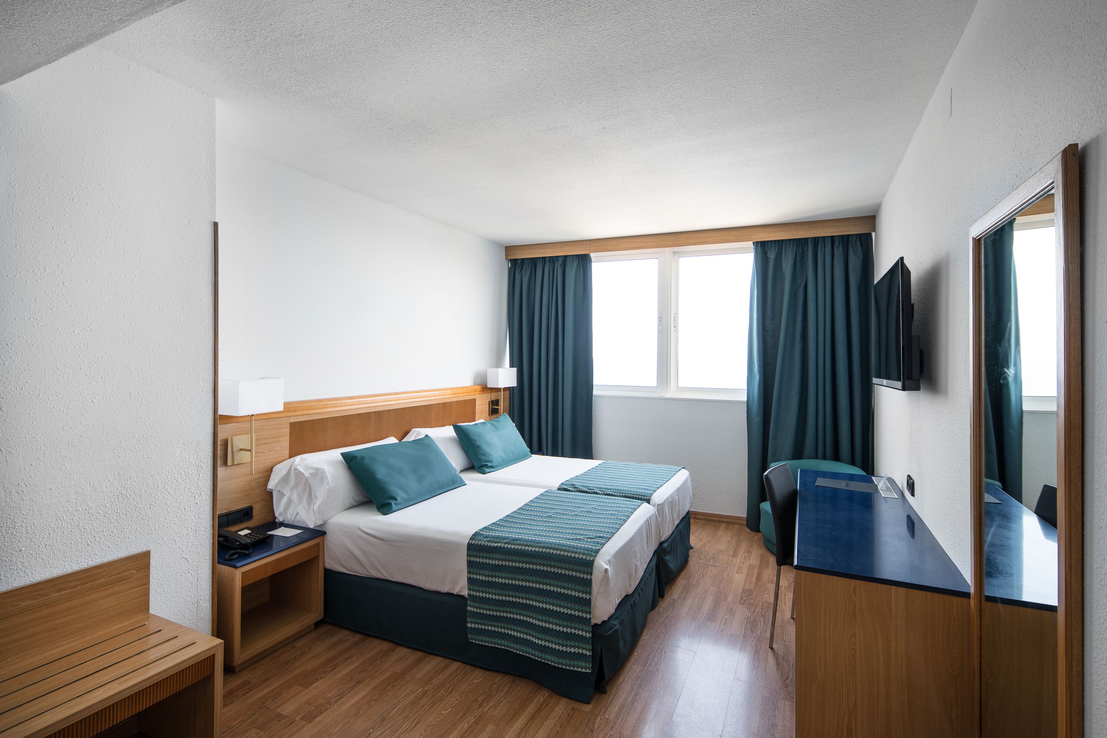 A hotel room with a bed, bedside table, desk, and a TV.