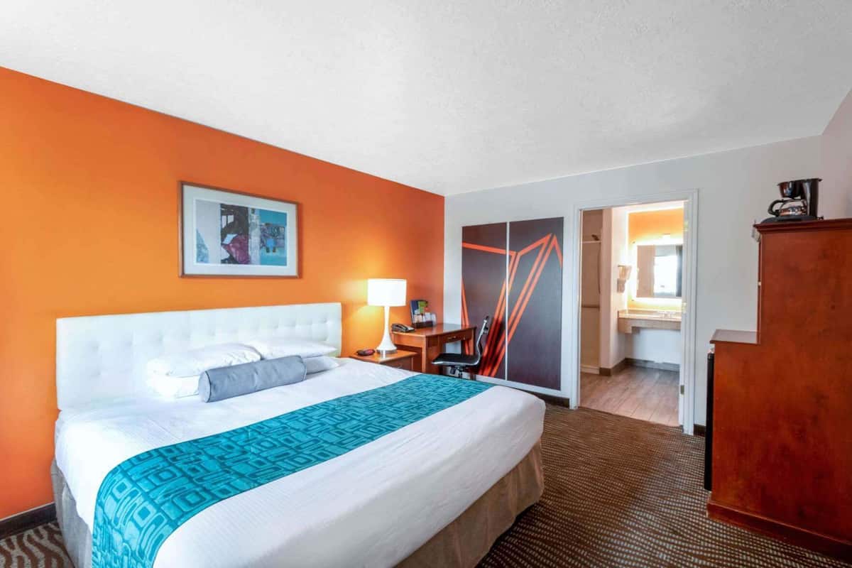 Ein Hotelzimmer mit Bett, Schreibtisch, Stuhl, Kleiderschrank und einem durchgegangenen Tür sichtbaren Badezimmer.