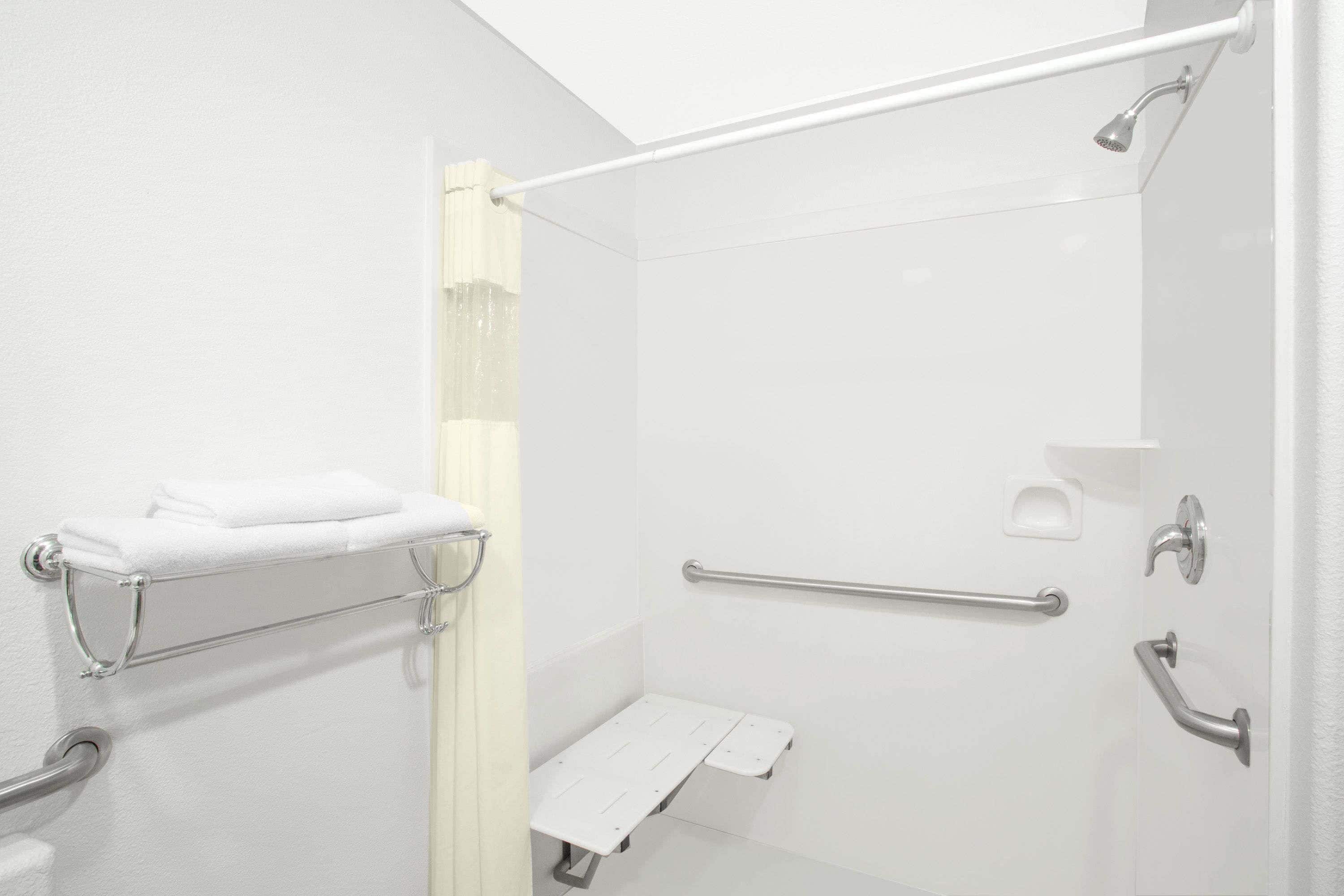 A modern bathroom with a walk-in shower, grab bars, a towel rack, and a toilet with a safety bar.