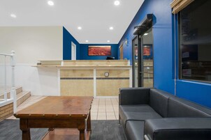 Zona de recepción con mostrador de madera, sofá de cuero negro y piso de baldosas.