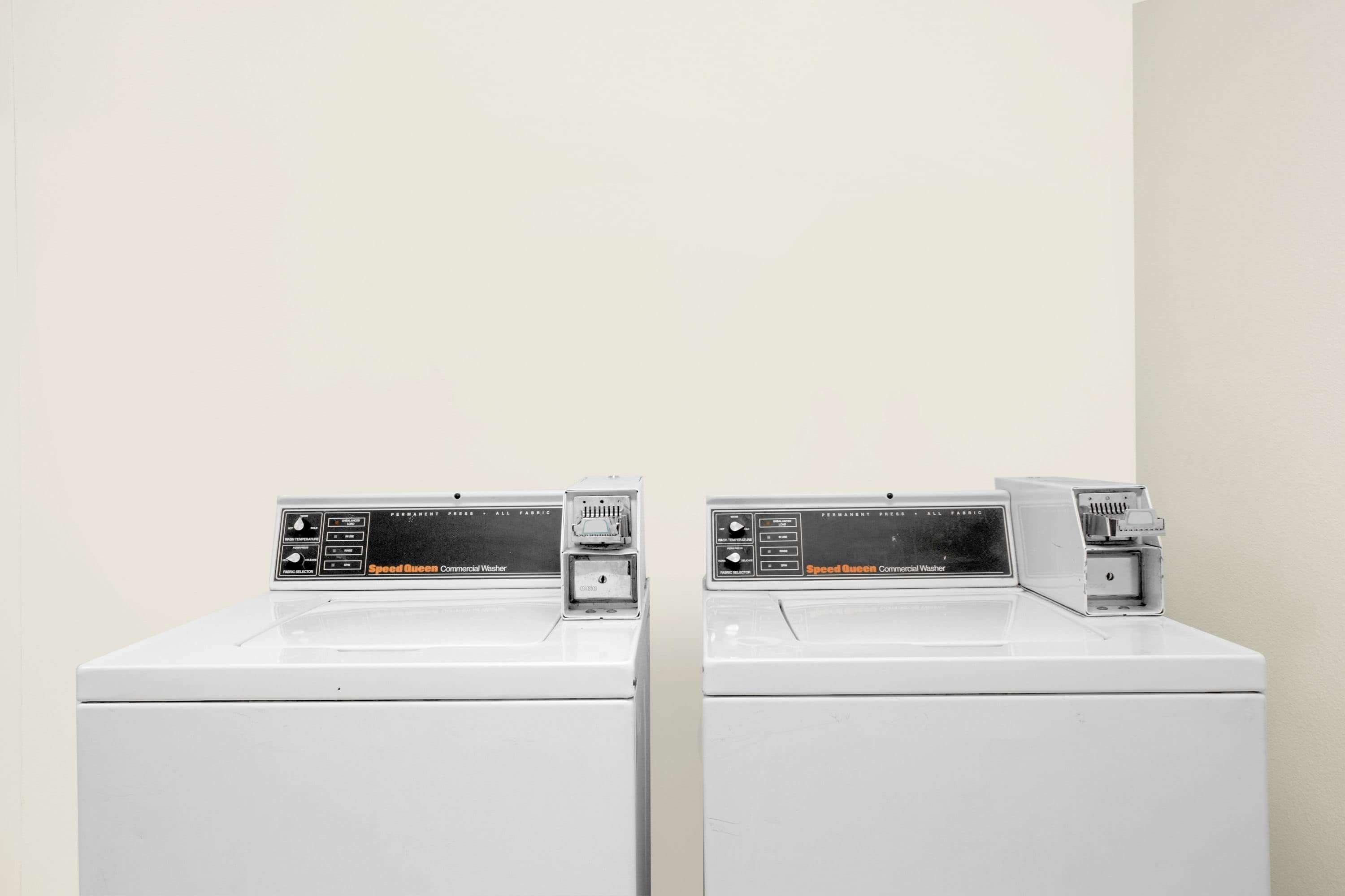 Two identical commercial washers with control panels, placed side by side against a plain wall.