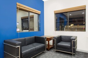 Una habitación con una pared azul, dos sofás de cuero negro, una mesa de madera y una ventana con persianas.