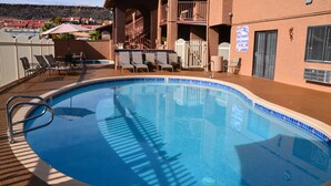 A swimming pool with a tiled edge, surrounded by lounge chairs and a covered seating area.