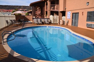 Una piscina con borde de azulejos, rodeada de sillones de descanso y una zona de estar cubierta.