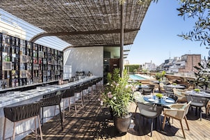 Um bar no terraço com um balcão comprido, banquetas e mesas ao ar livre.