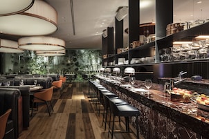 Uma área de bar moderna com assentos de couro, bancada de mármore e vista para o verde através do muro de vidro.