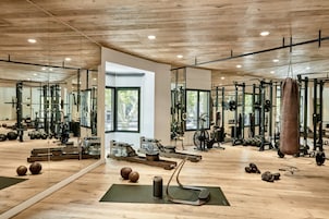 Uma academia com piso de madeira, diversos equipamentos de exercício e grandes espelhos.
