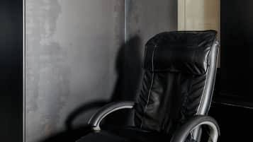 A black leather reclining chair with armrests, positioned against a textured wall with a mix of dark and light areas.