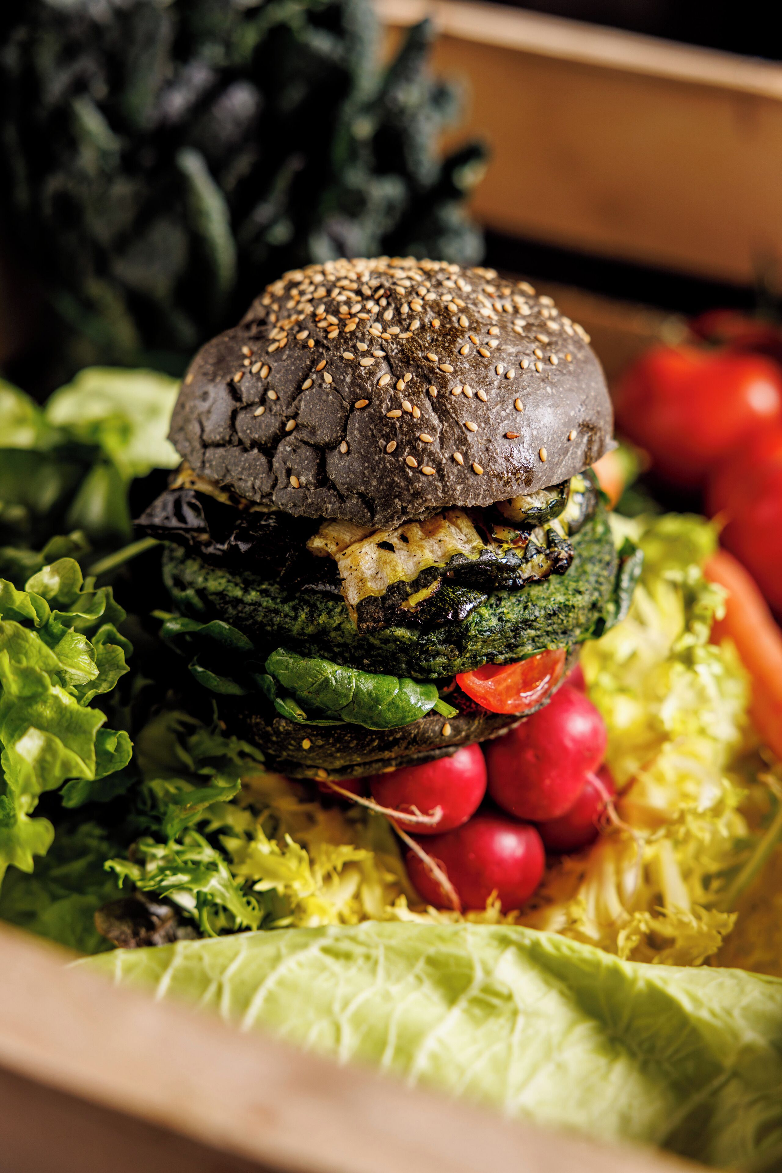 Un primo piano di un hamburger con pane ai semi di sesamo, circondato da verdure fresche.
