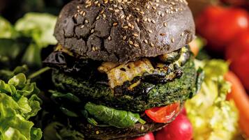 Un primo piano di un hamburger con pane ai semi di sesamo, circondato da verdure fresche.