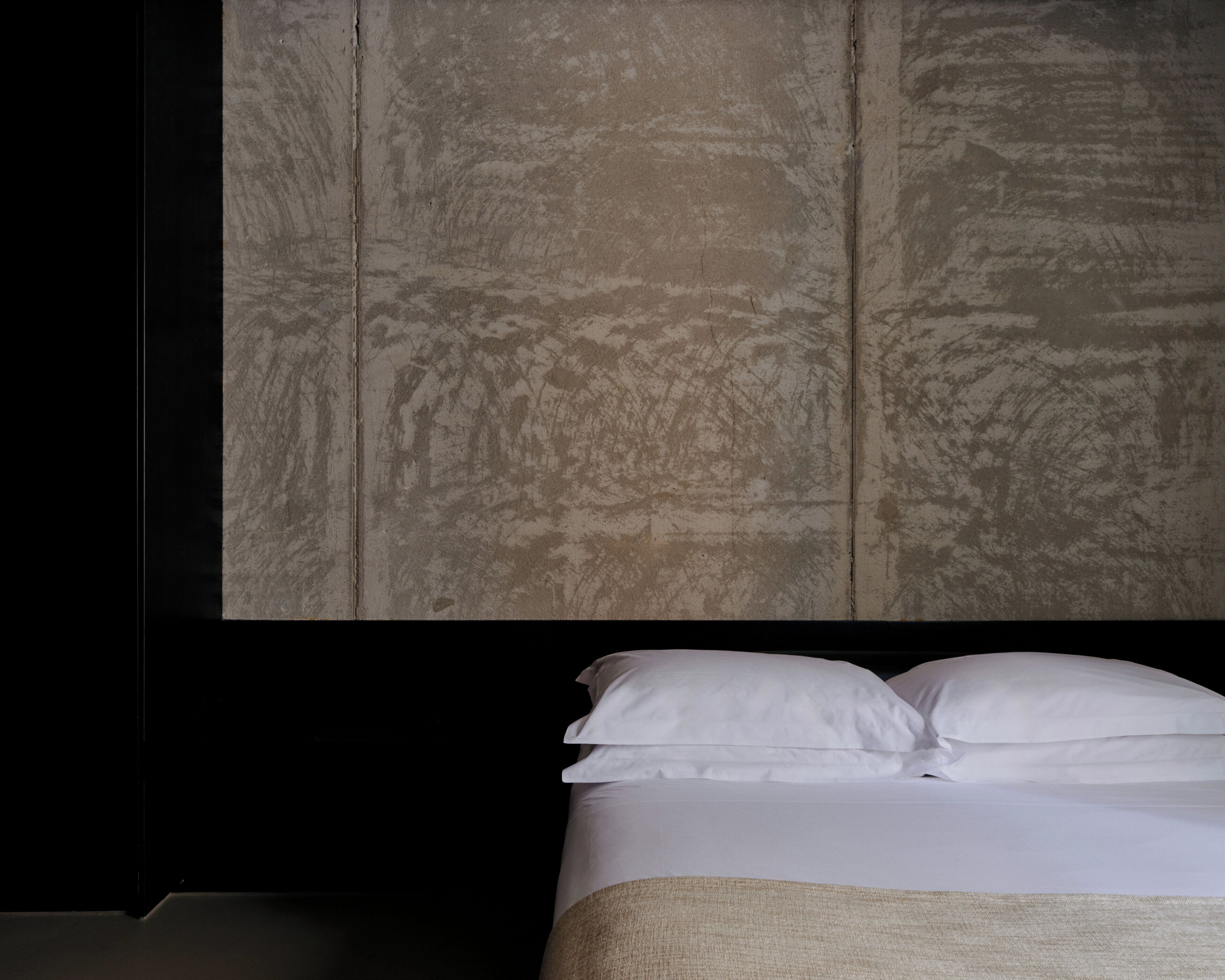 Una habitación con cama, ropa de cama blanca y pared texturizada.
