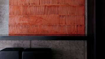 A modern hotel room with a large, textured orange wall, a bed with a beige cover, and black headboards.