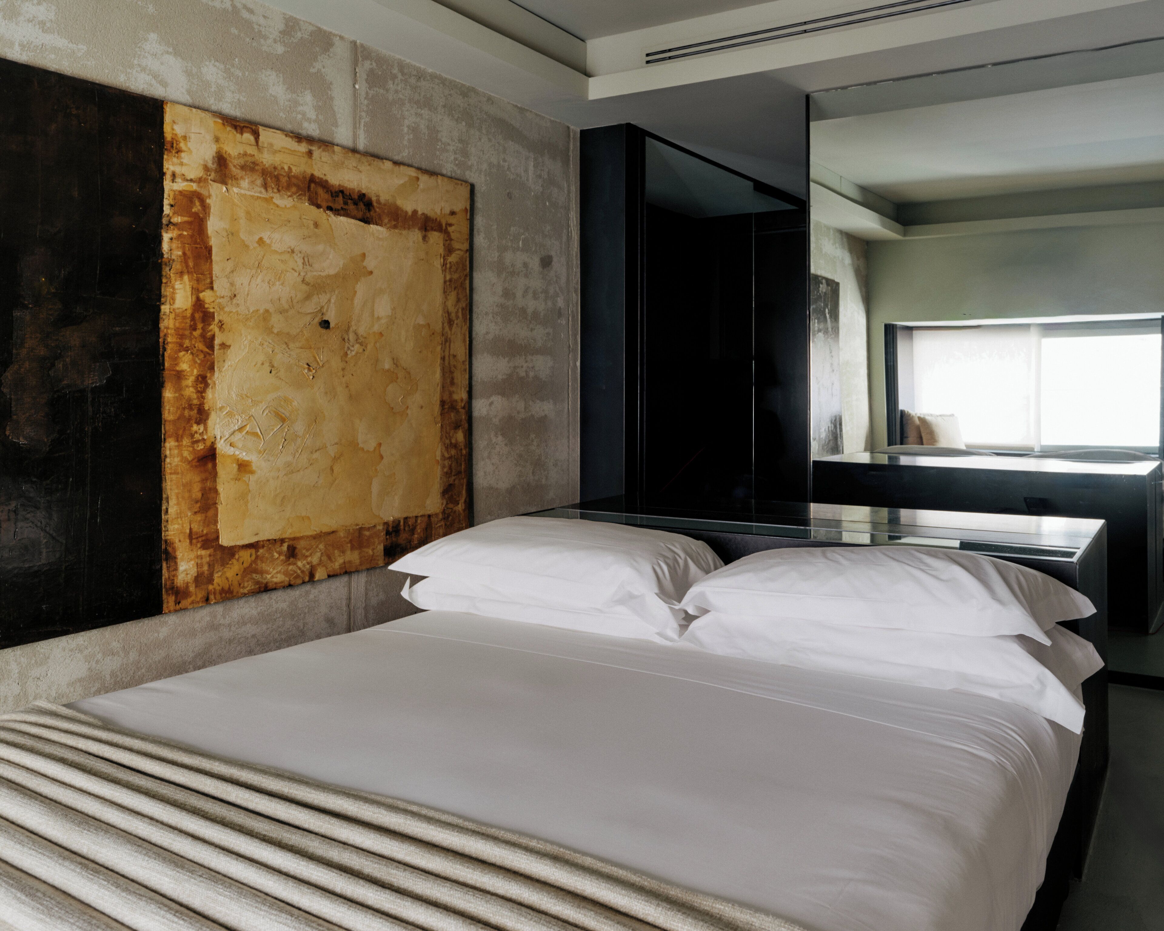 A modern hotel room with a large bed, a dark wardrobe, and a large artwork on the wall.