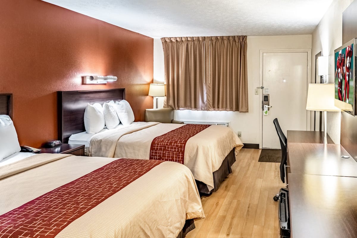 A hotel room with two beds, a desk, a chair, a TV, and a window with curtains.