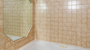 Een badkamer met een bad, een spiegel en beige betegelde wanden.