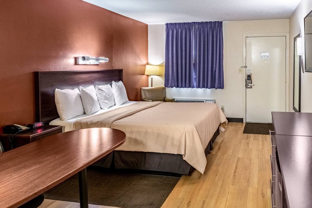 Una habitación de hotel con cama, mesita de noche, lámpara y una puerta.