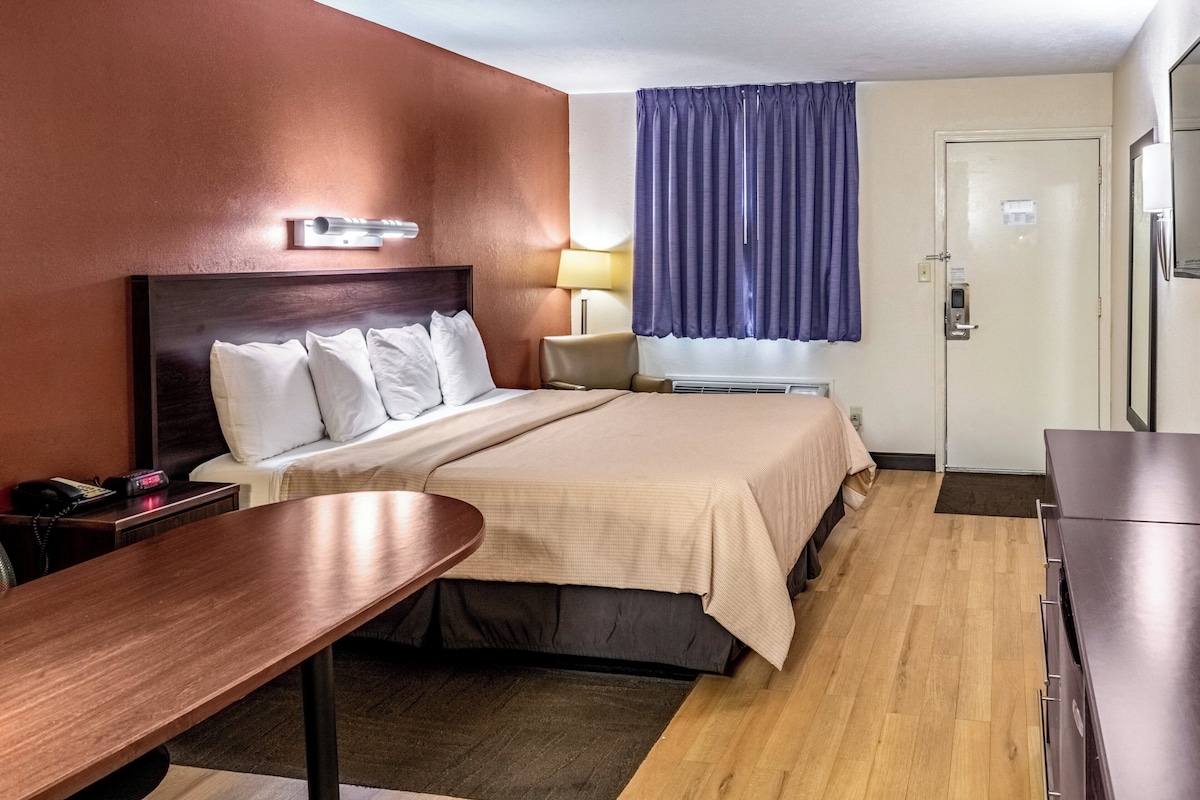 Una habitación de hotel con cama, escritorio, silla, lámpara y puerta.