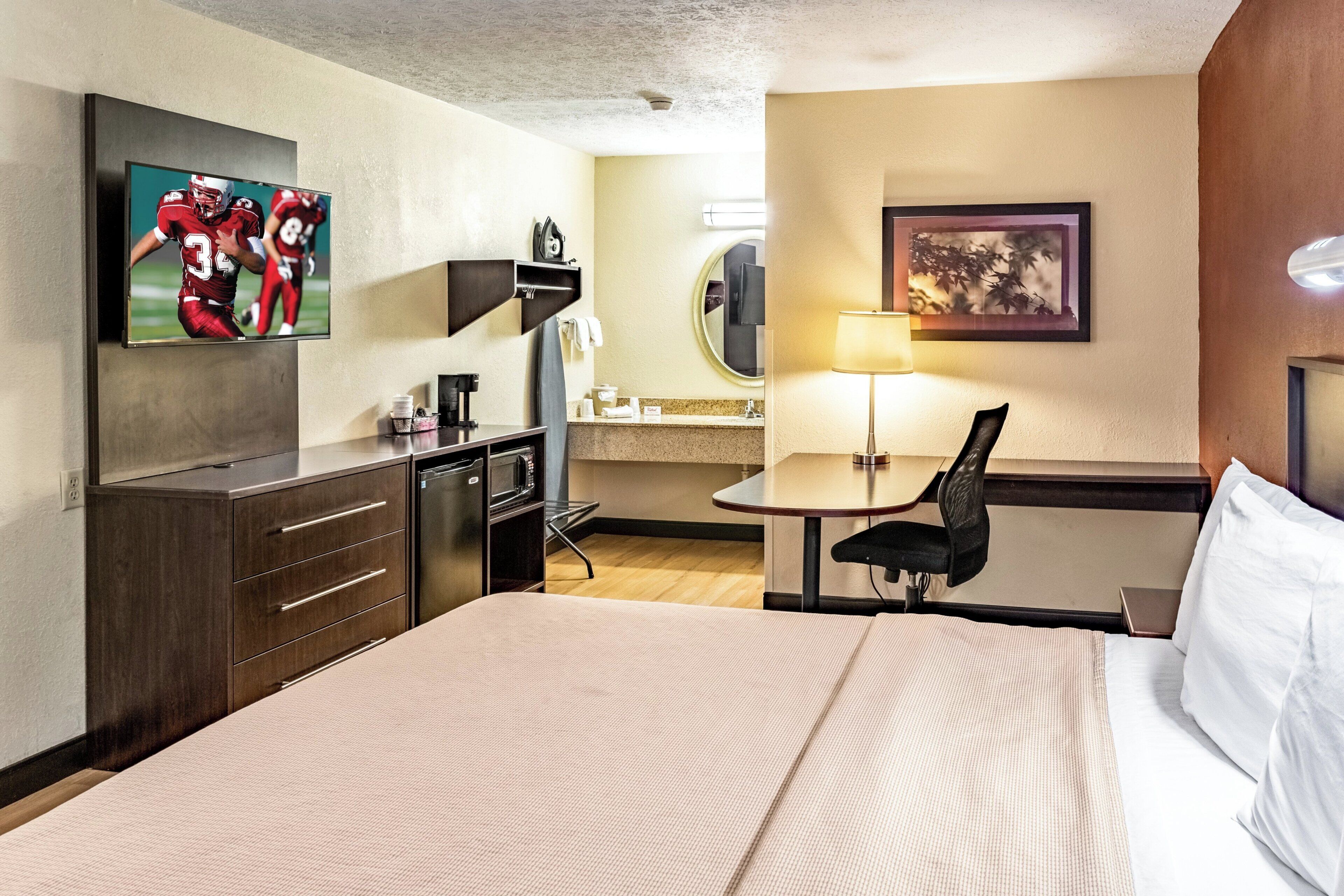 Ein Hotelzimmer mit einem Bett, einem Schreibtisch, einem Stuhl, einem Fernseher, einem Spiegel und einer Lampe.