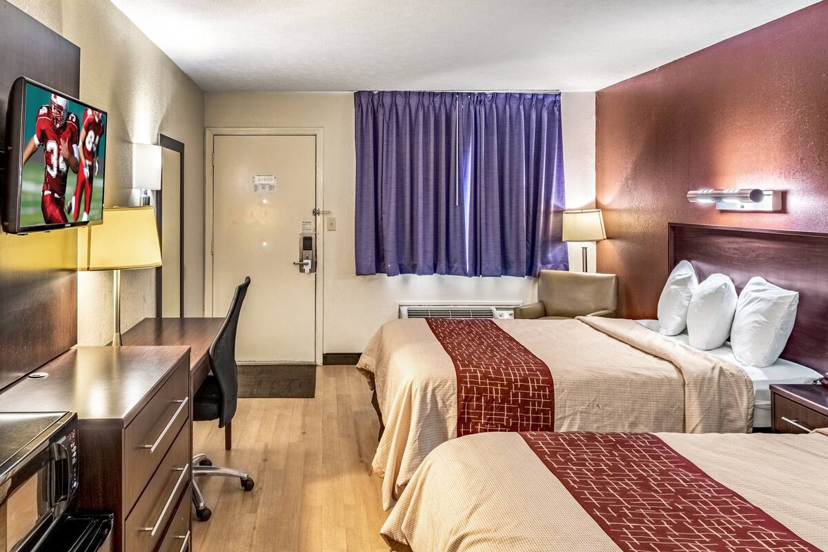 Habitación de hotel con dos camas, un escritorio con computadora, televisión y ventana con cortinas.