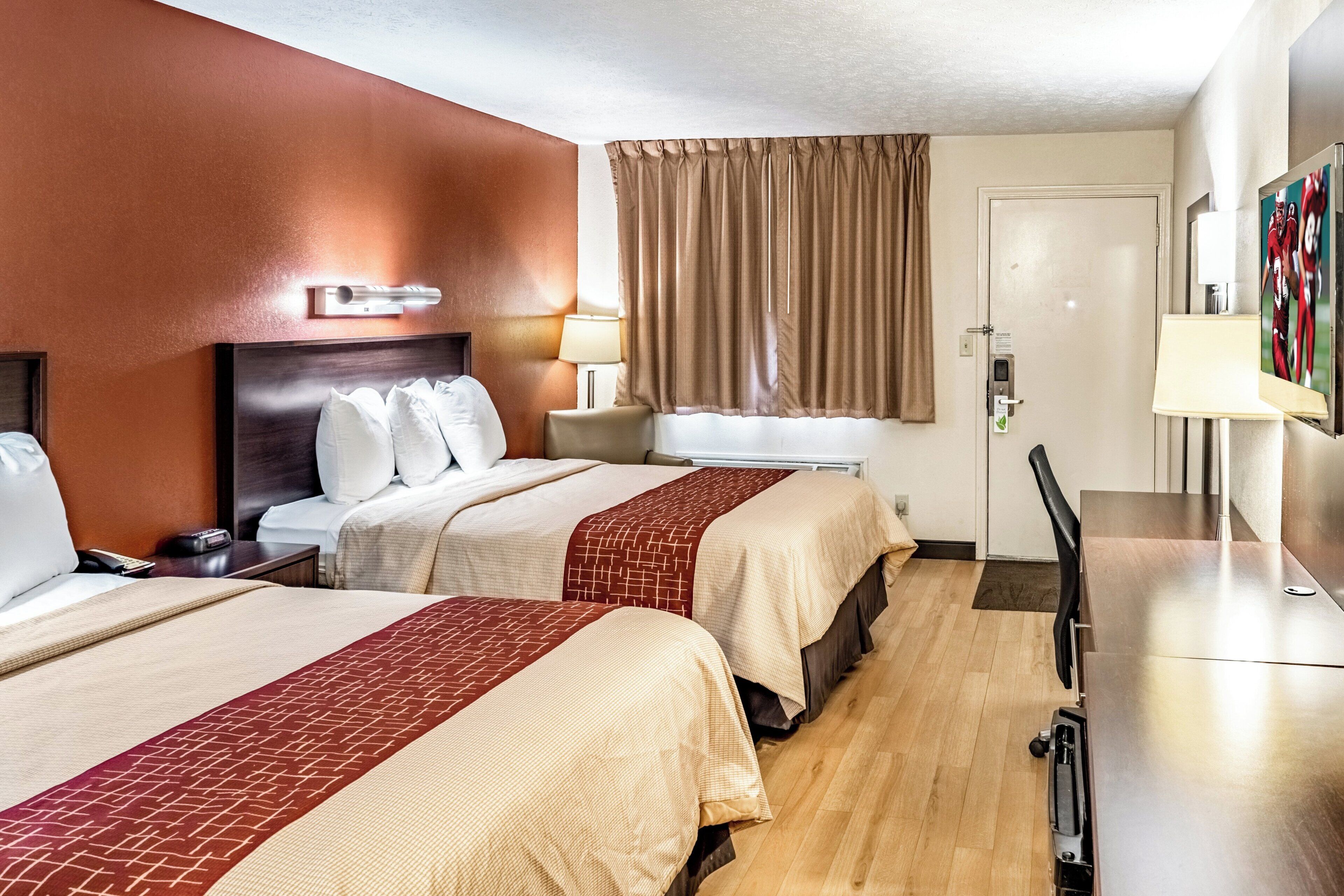 Habitación de hotel con dos camas, un escritorio, una silla, una lámpara, una ventana con cortinas y una puerta.
