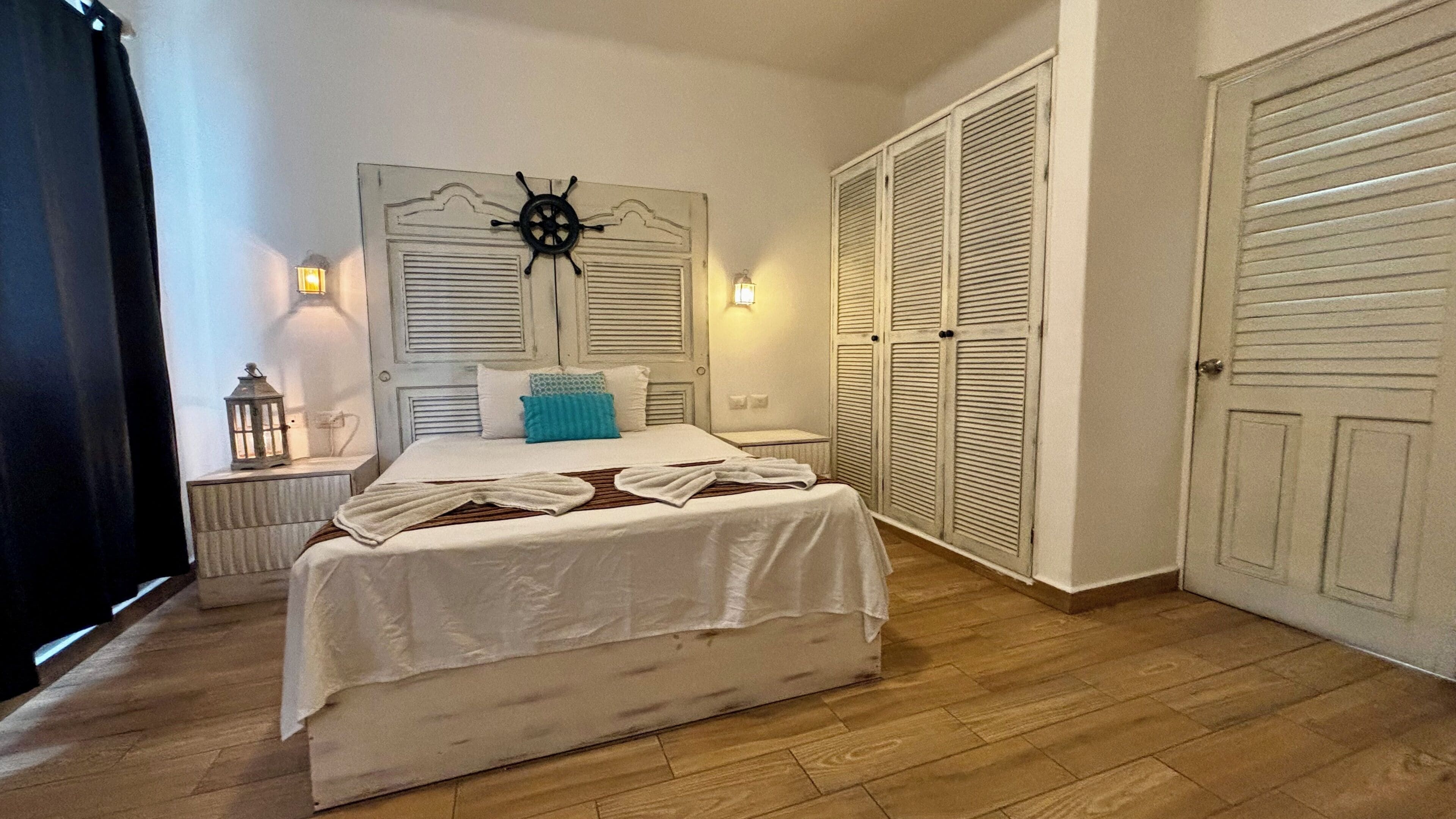 A bedroom with a bed, bedside lamps, a ship's wheel decoration, and a wardrobe.