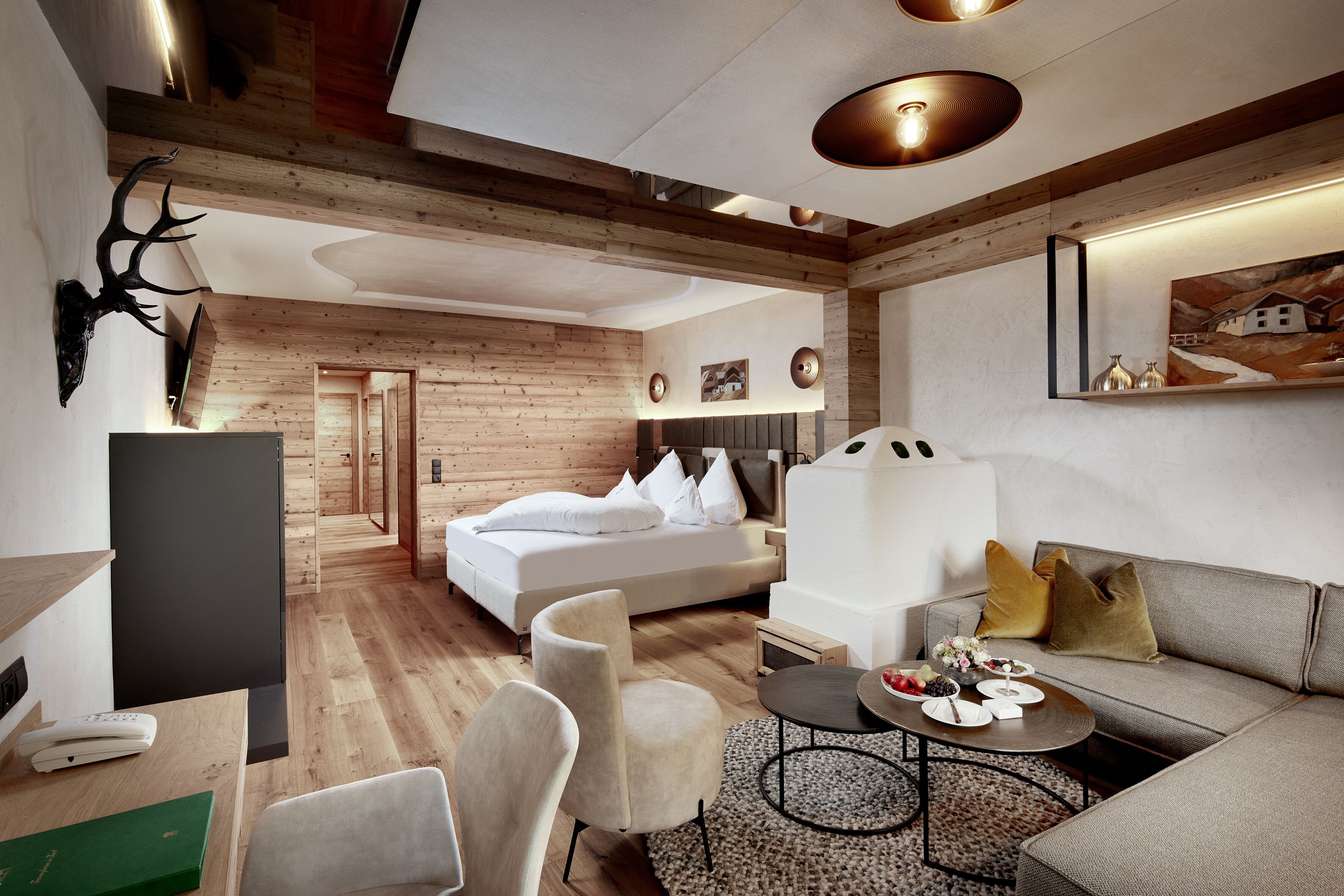 A modern hotel room with a wooden ceiling, a bed with white bedding, a sofa, a coffee table, and a TV.