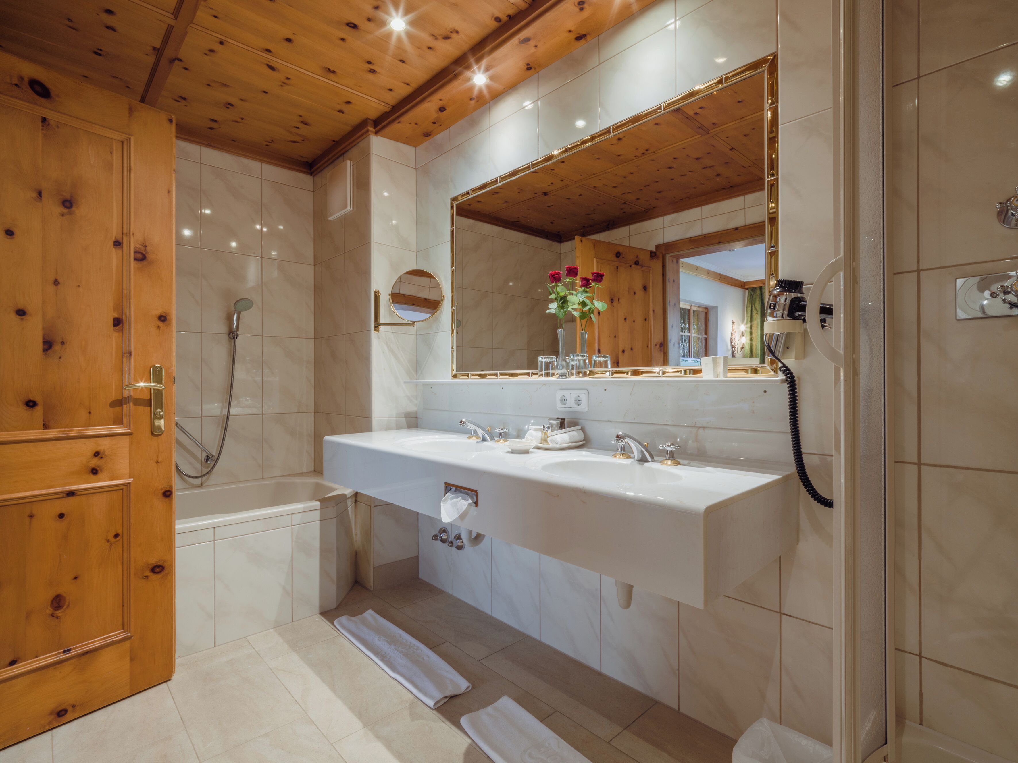 Ein modernes Badezimmer mit Holzboden, einem Doppelwaschbecken, einem Spiegel und einer Dusche.