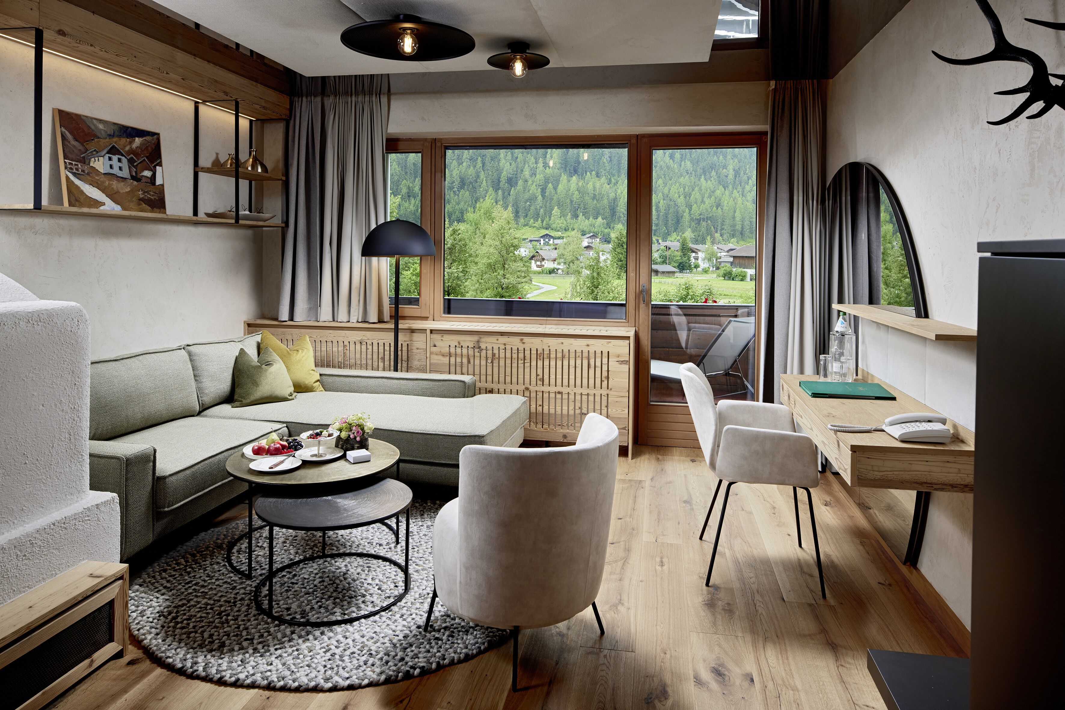 Ein modernes Wohnzimmer mit einer Couch, Sesseln, einem Esstisch und Blick auf eine bewaldete Landschaft durch große Fenster.