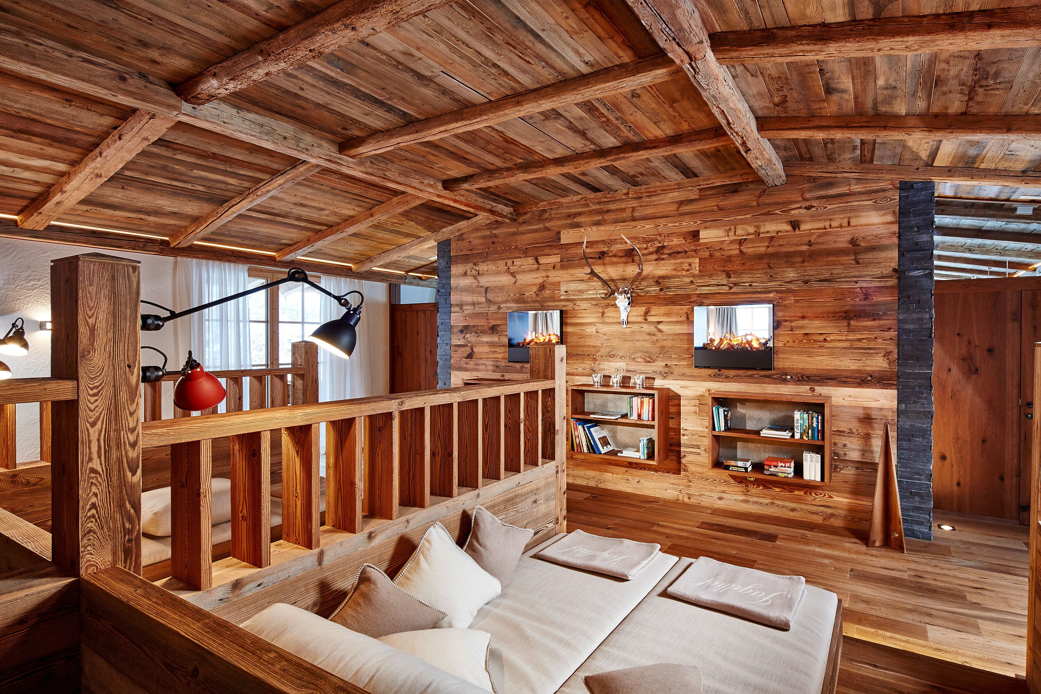 A rustic wooden cabin interior with a bed, bookshelves, and a fireplace.