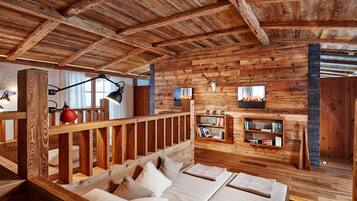 A rustic wooden cabin interior with a bed, bookshelves, and a fireplace.
