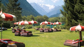 Outdoor lounge chairs and umbrellas in a grassy area with mountains in the background.