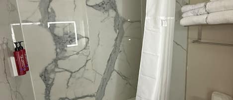 Un baño con pared de ducha de mármol, un inodoro blanco y un toallero con toallas dobladas.
