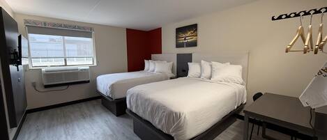 A hotel room with two beds, a window with a view, a radiator, and a coat rack.