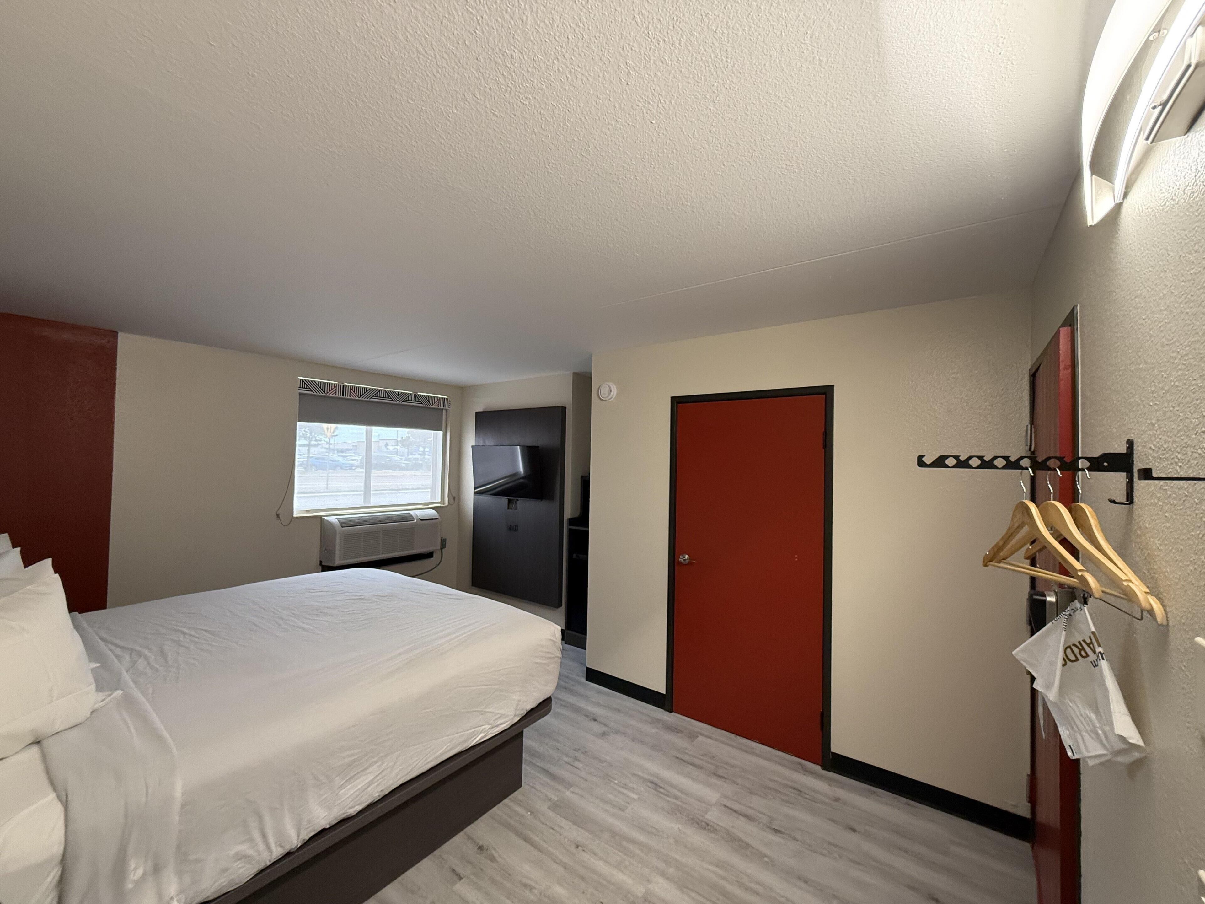 A hotel room with a bed, a wardrobe, a mirror, and a window with a view of the outside.