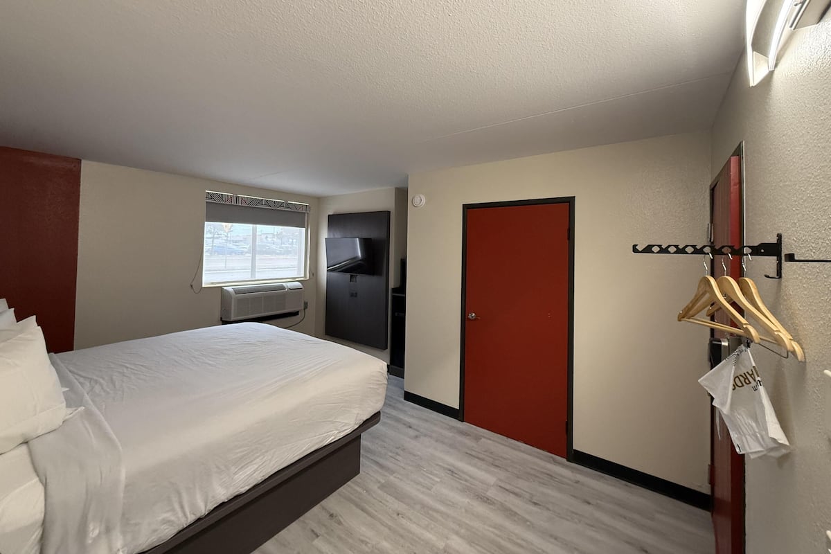 Habitación de hotel con cama, armario, espejo y ventana con vistas al exterior.