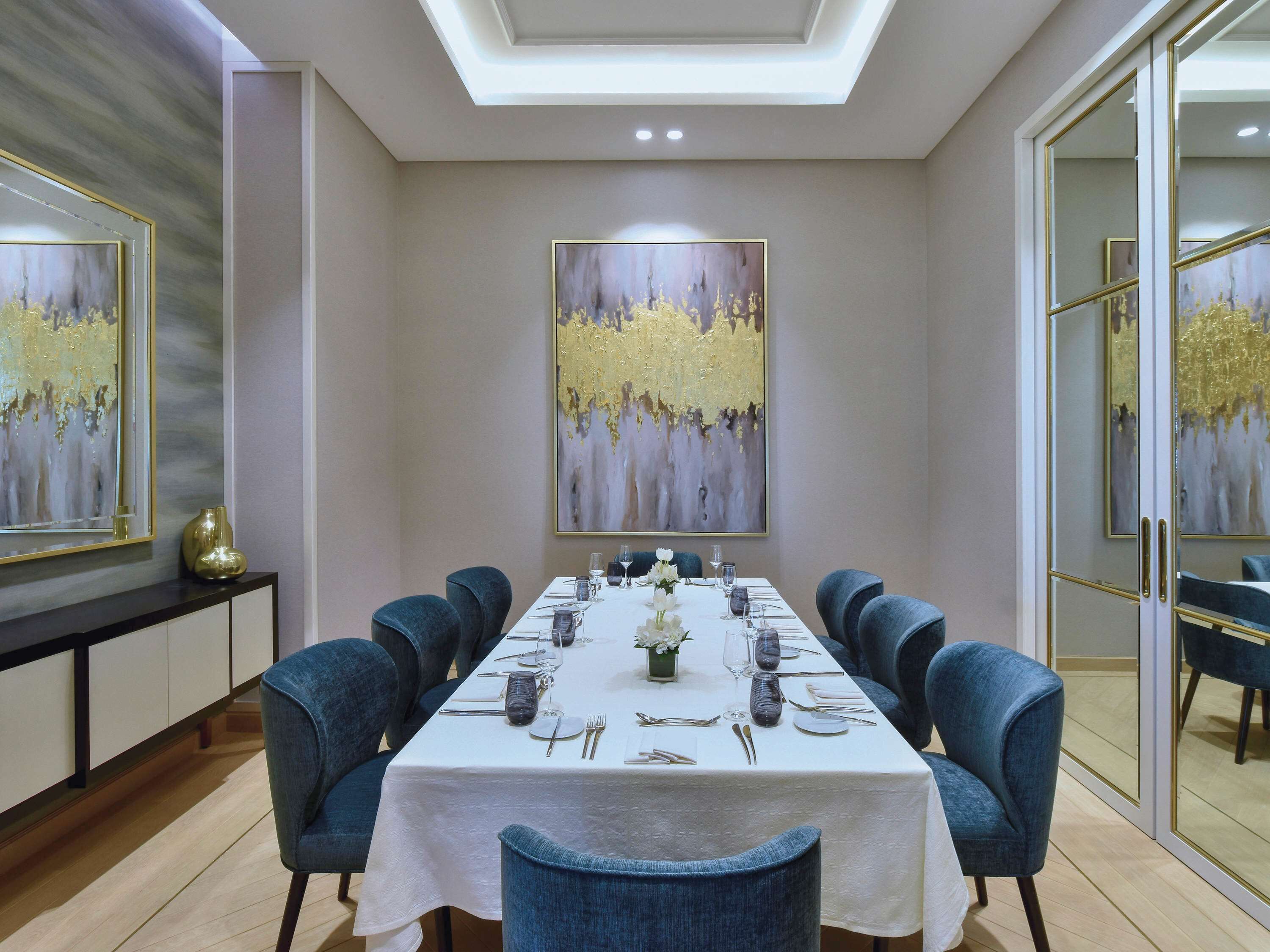 A dining area with a long table set for six, surrounded by six blue chairs.