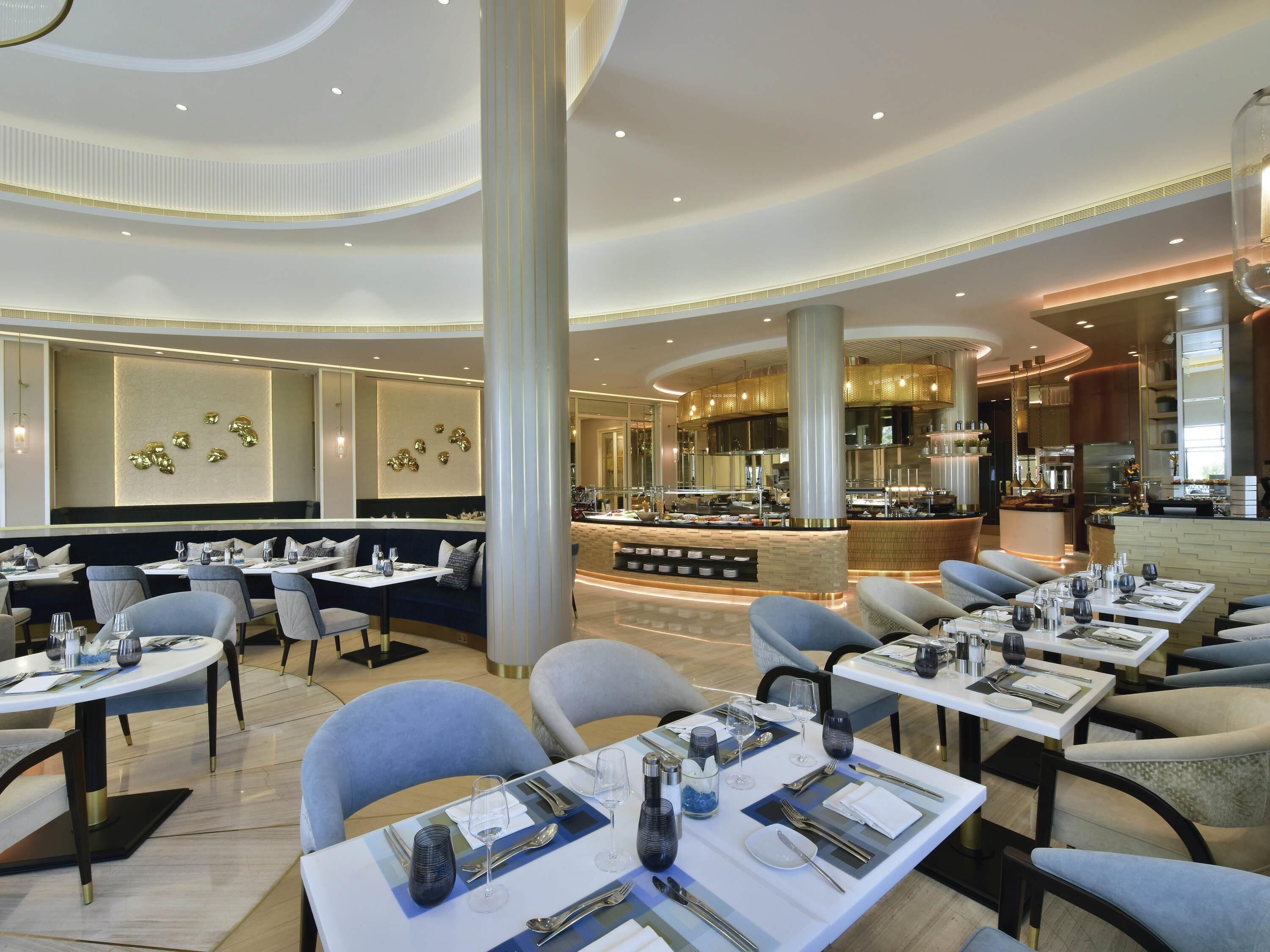 A modern restaurant with round tables, high ceilings, and a central bar area.