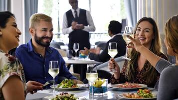 Un grupo de personas cenando en un restaurante, con un camarero al fondo.