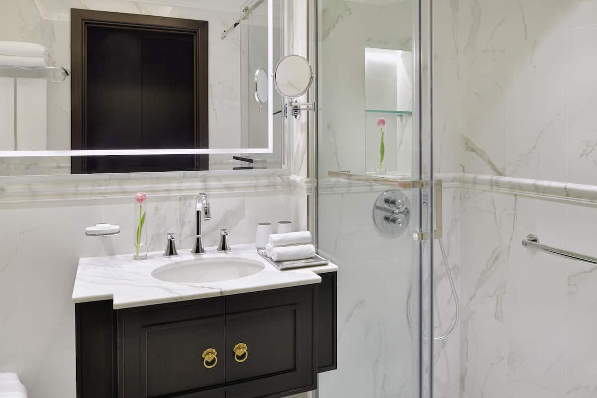 Un baño moderno con lavamanos de mármol, muebles de tono oscuro y cabina de ducha con mampara de vidrio.