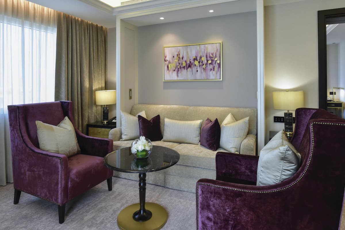 Una habitación de hotel moderna con un sofá, dos sillones, una mesita de centro y un cuadro en la pared.