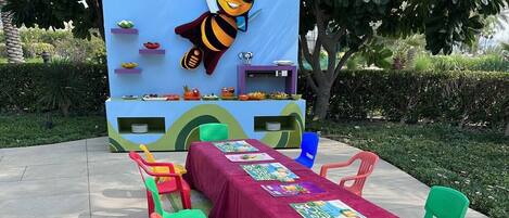 Un área de estar al aire libre con una mesa cubierta con mantel rojo, rodeada de sillas de plástico de colores.