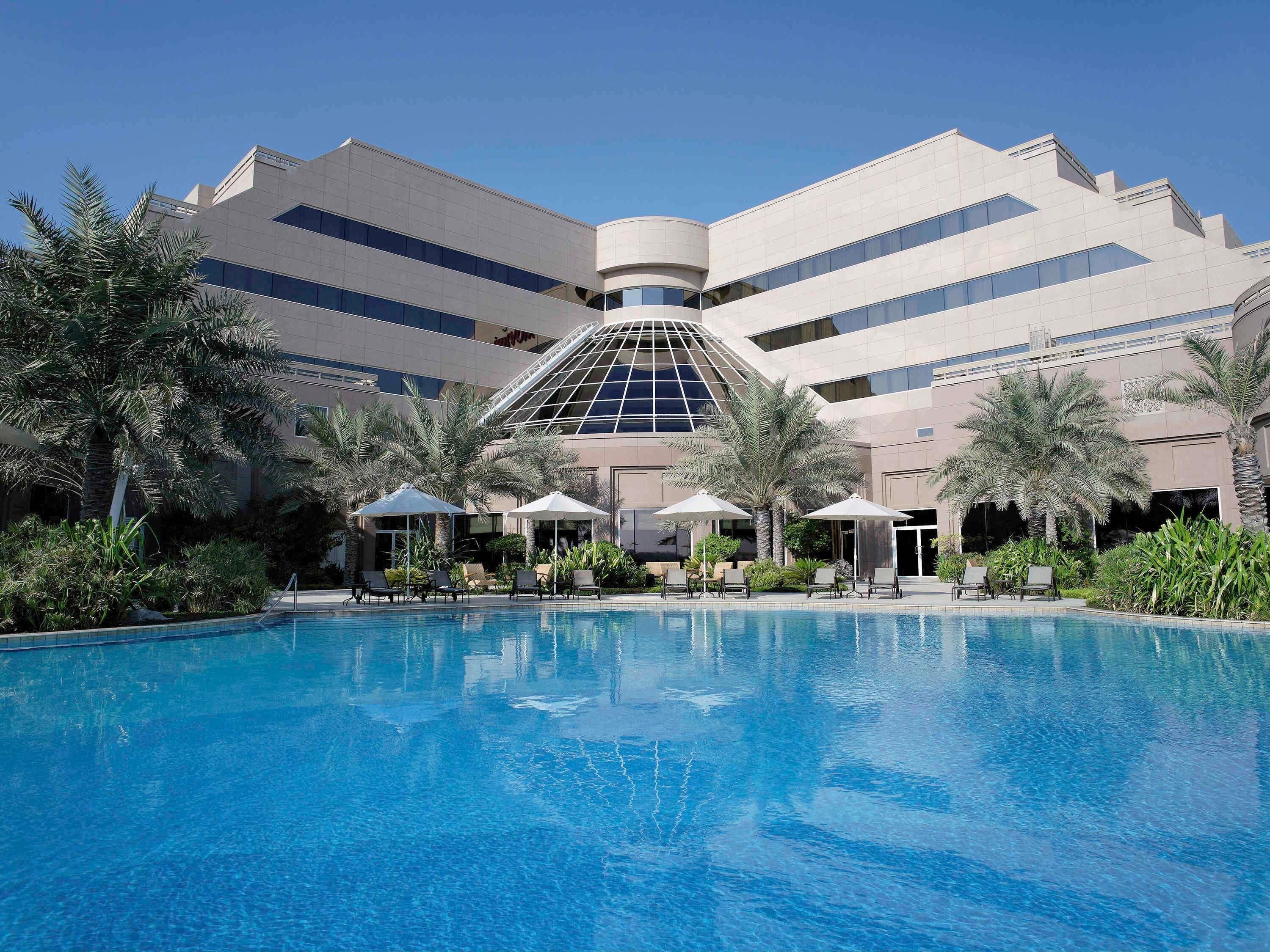 A modern hotel with a large pool, palm trees, and lounge chairs.