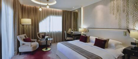 A hotel room with a large bed, two armchairs, a small table, and a desk.