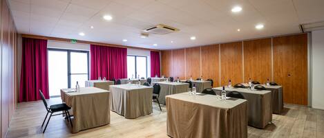 A conference room with multiple tables, chairs, and a large window with red curtains.