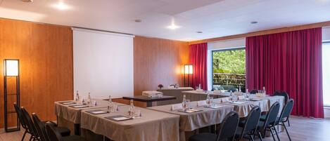 A conference room with tables, chairs, a projector screen, and a large window with curtains.