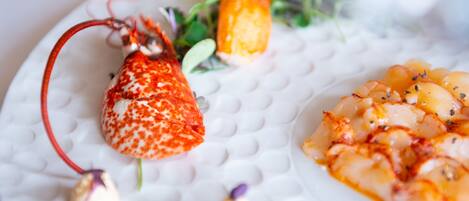 A white textured plate with a lobster tail, a piece of orange vegetable, and a seafood dish.